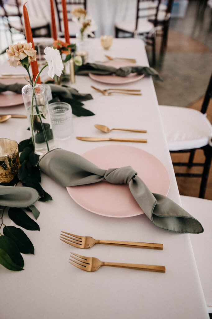 pink dinner plate with sage napkin, gold flatware and assorted bud vases and candles