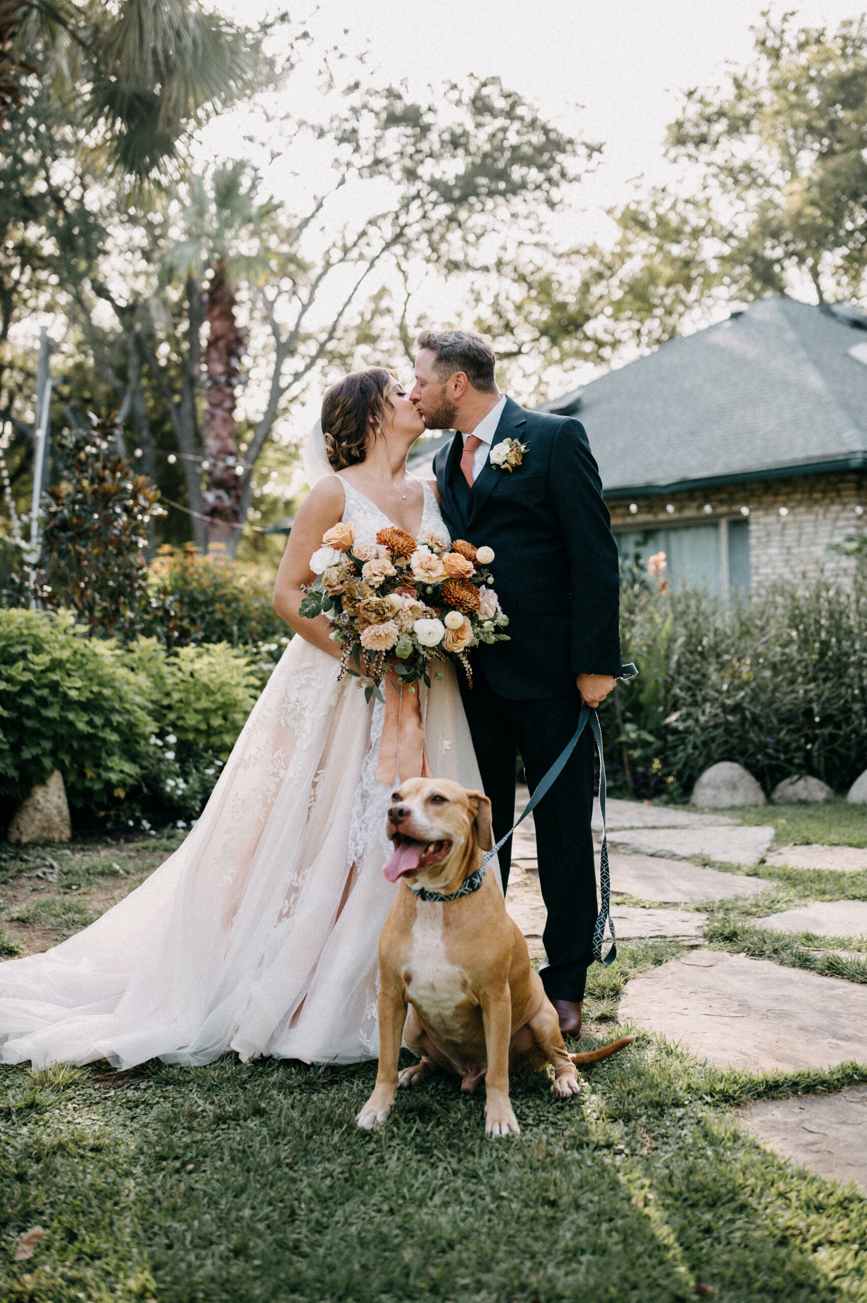 Bride and groom kissing with their dog on wedding day