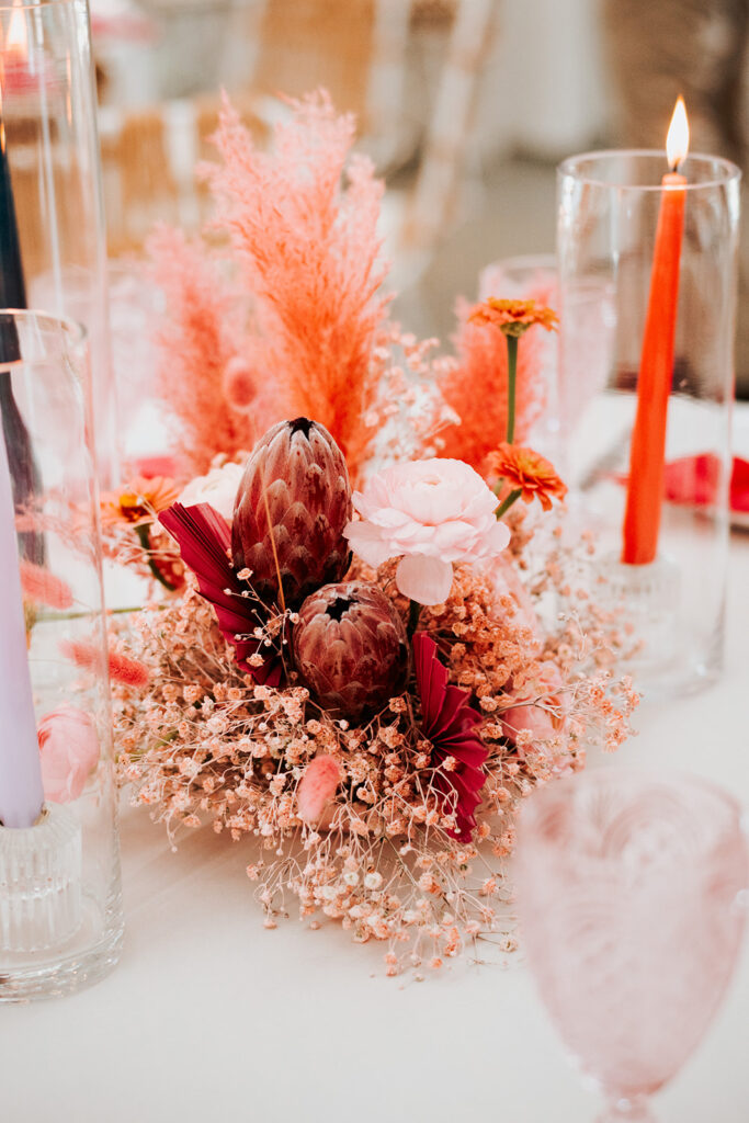 Bright pink and orange wedding centerpiece, with dried florals and taper candles

