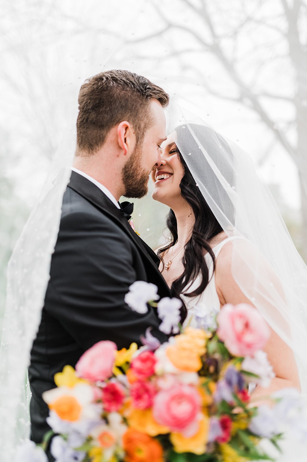 Newlyweds under the veil with colorful bridal bouquet