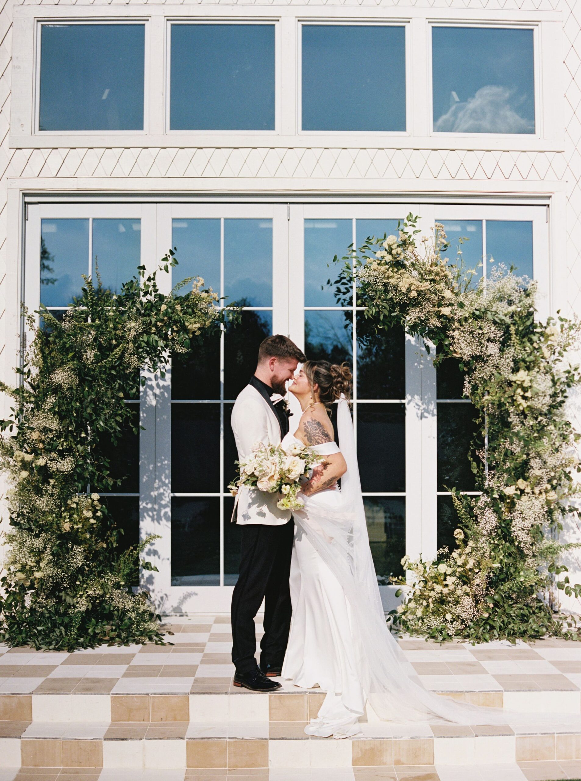 Bride and groom kissing in front of an asymmetrical floral arch