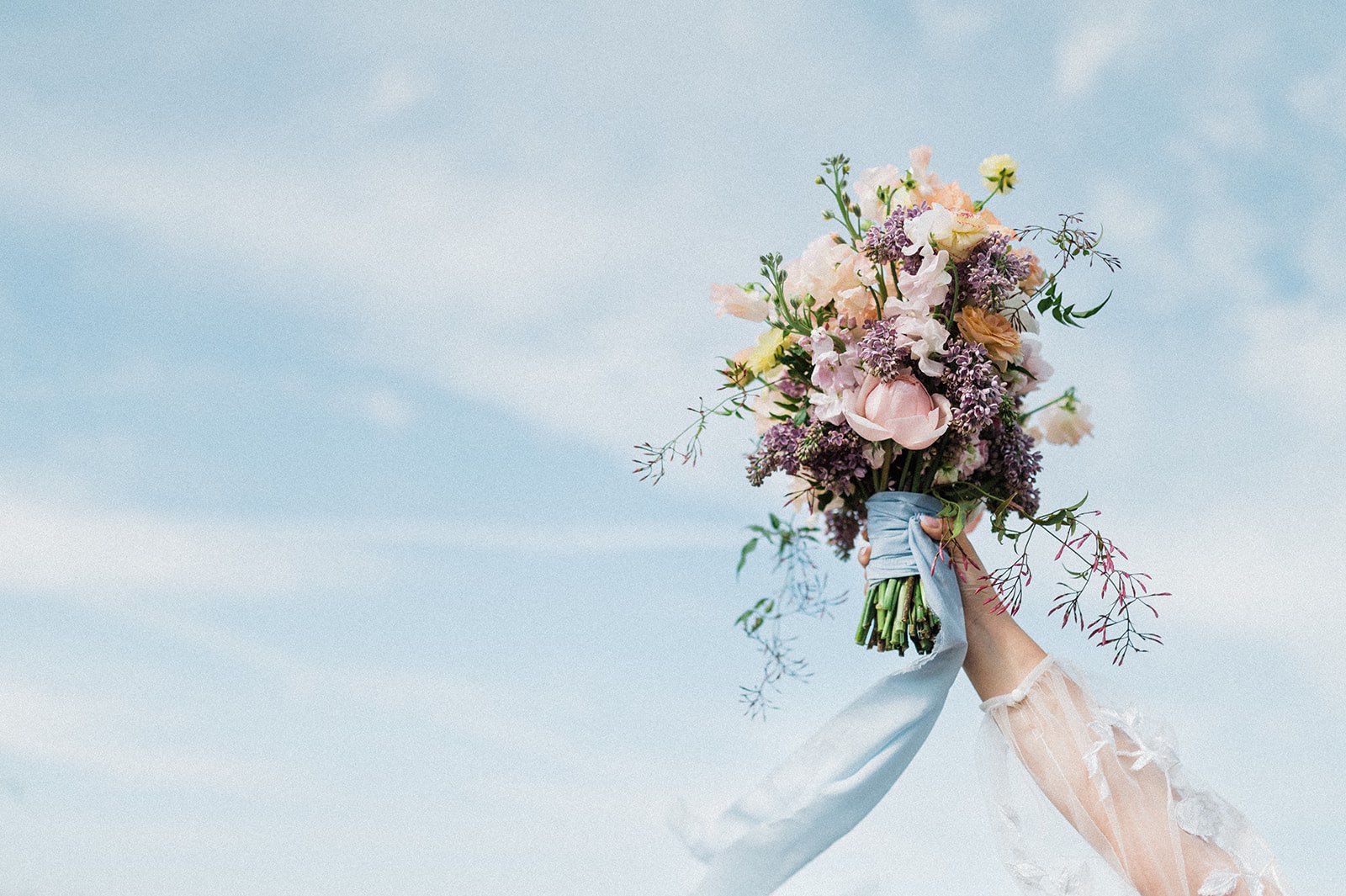pastel bridal bouquet with pale blue ribbon against the sky