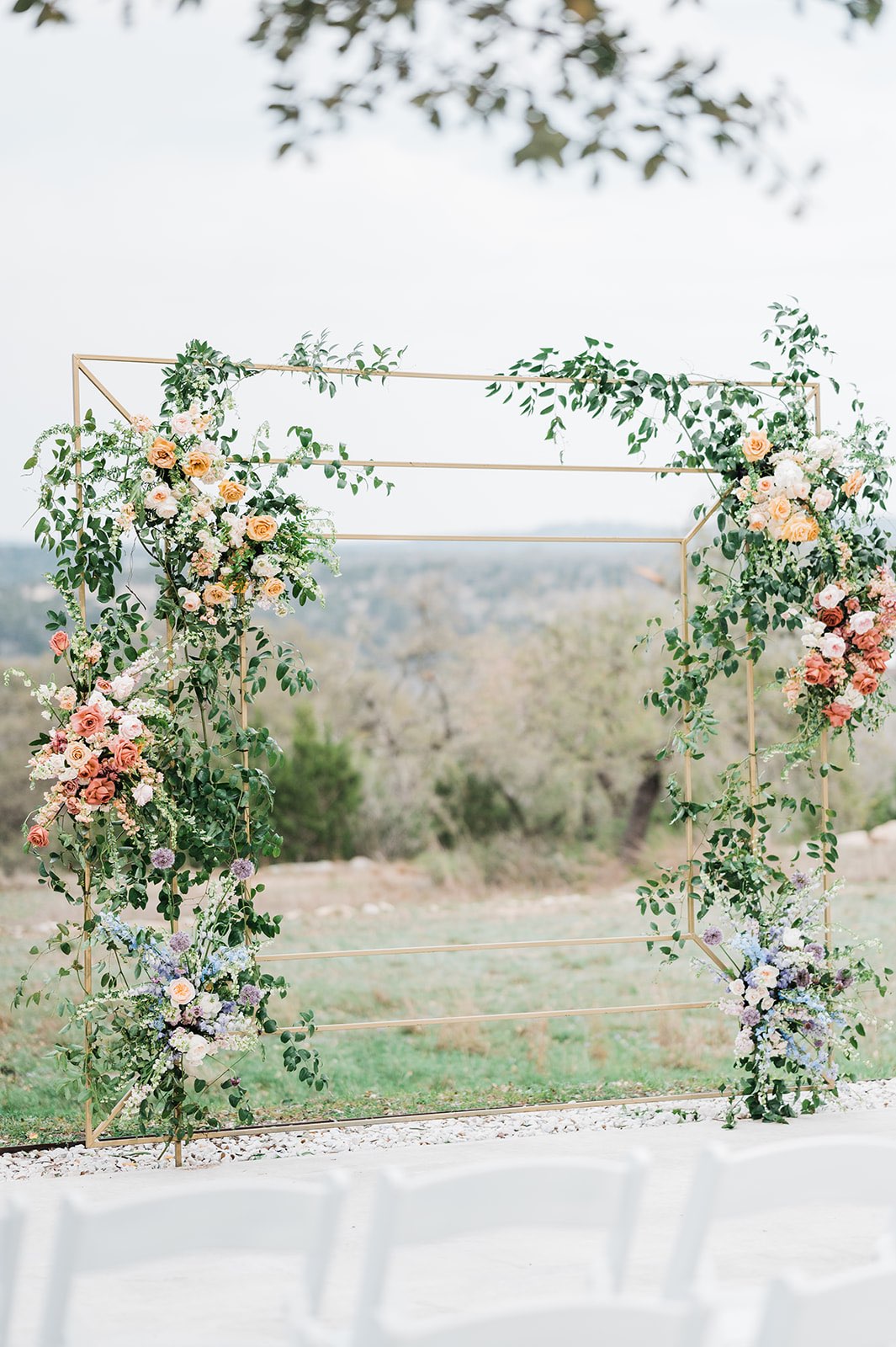 Pastel flowers and greenery on a square gold wedding arch 