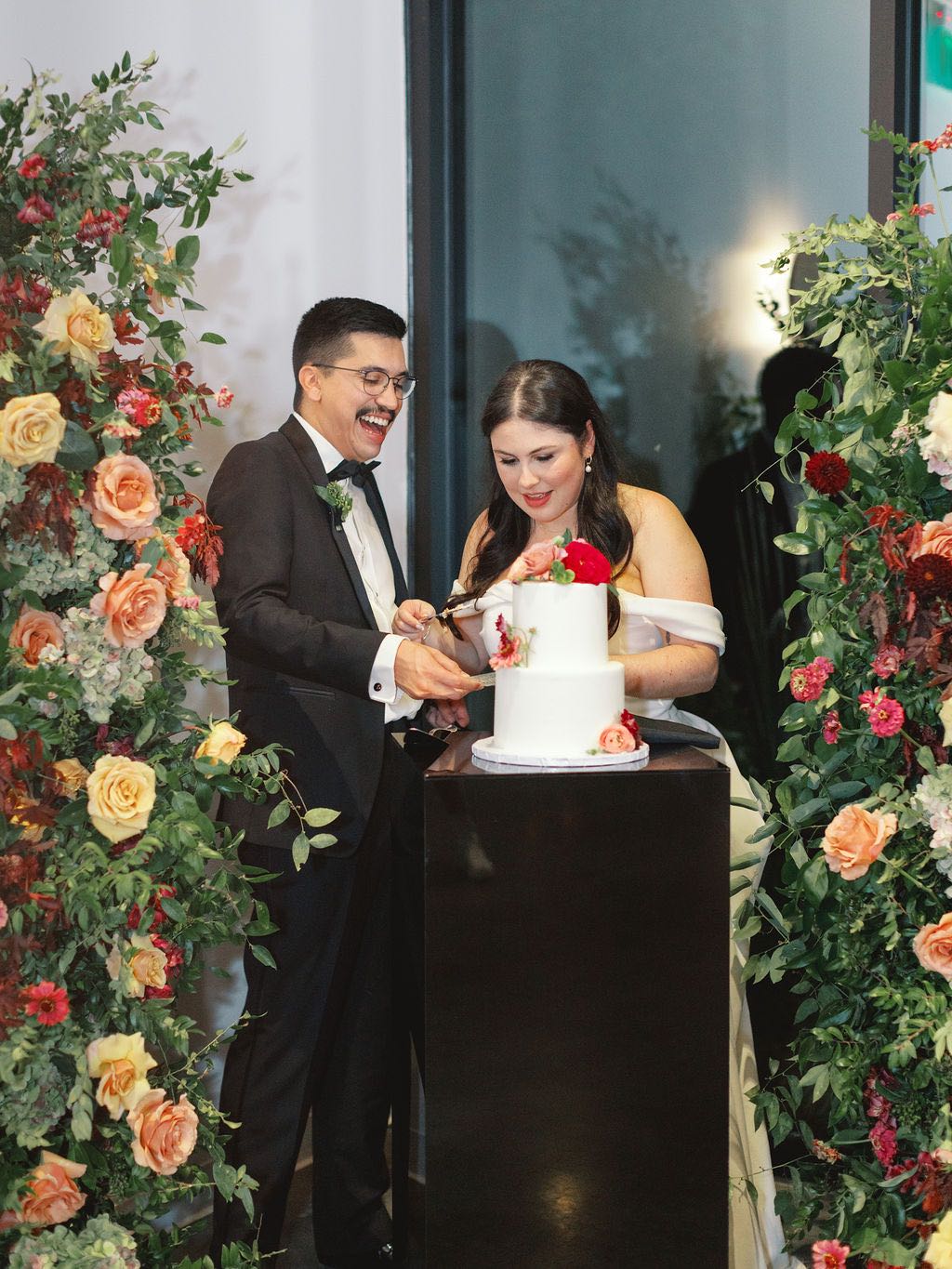 Couple cutting their cake surrounded by colorful plum and burgundy flowers