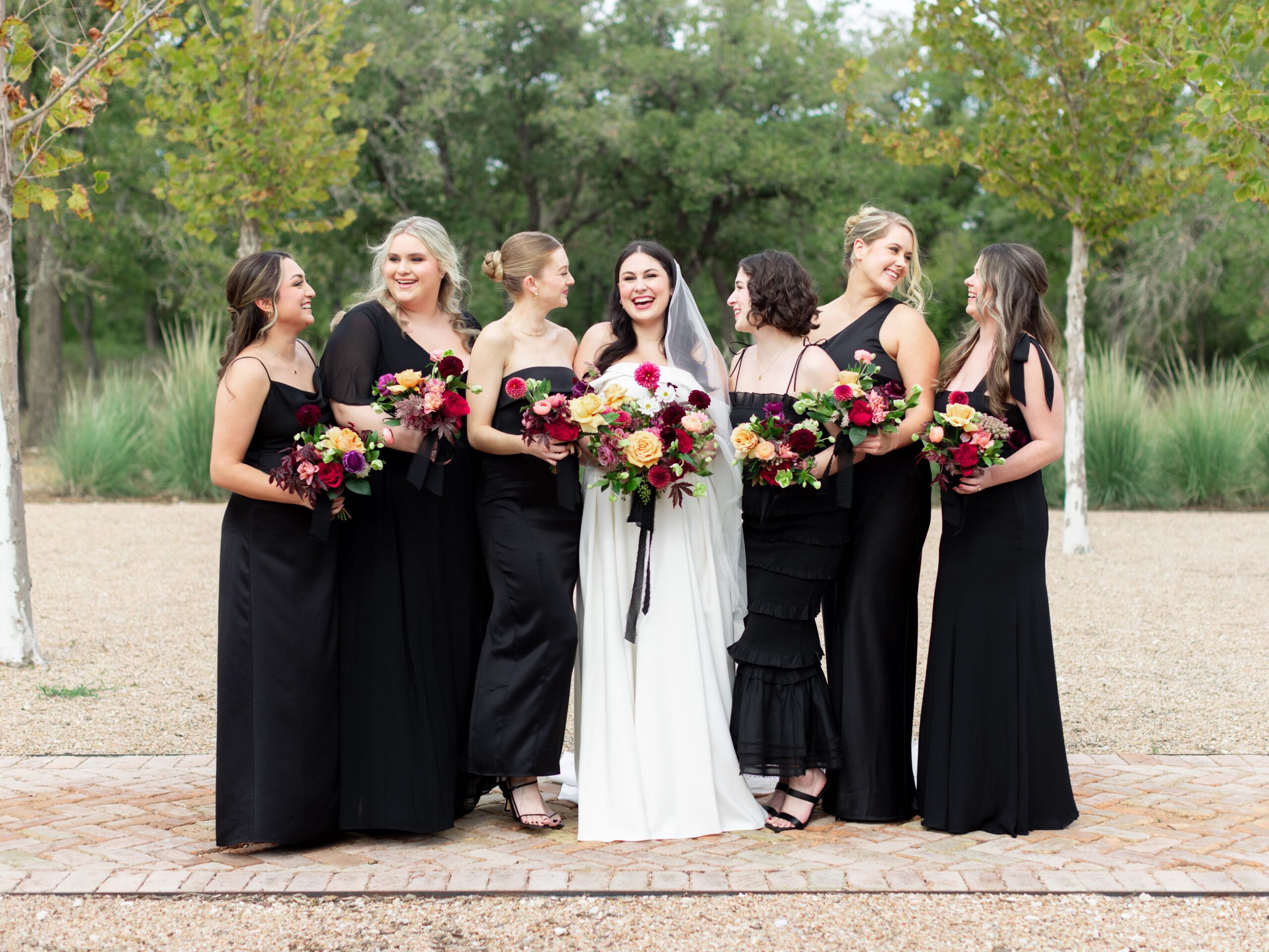 Bride with bridesmaids in mismatched black gowns with plum bouquets