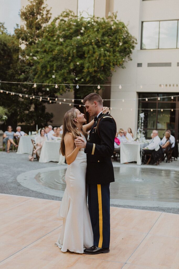 bride and groom in army uniform having first dance under bistro lighting in museum courtyard