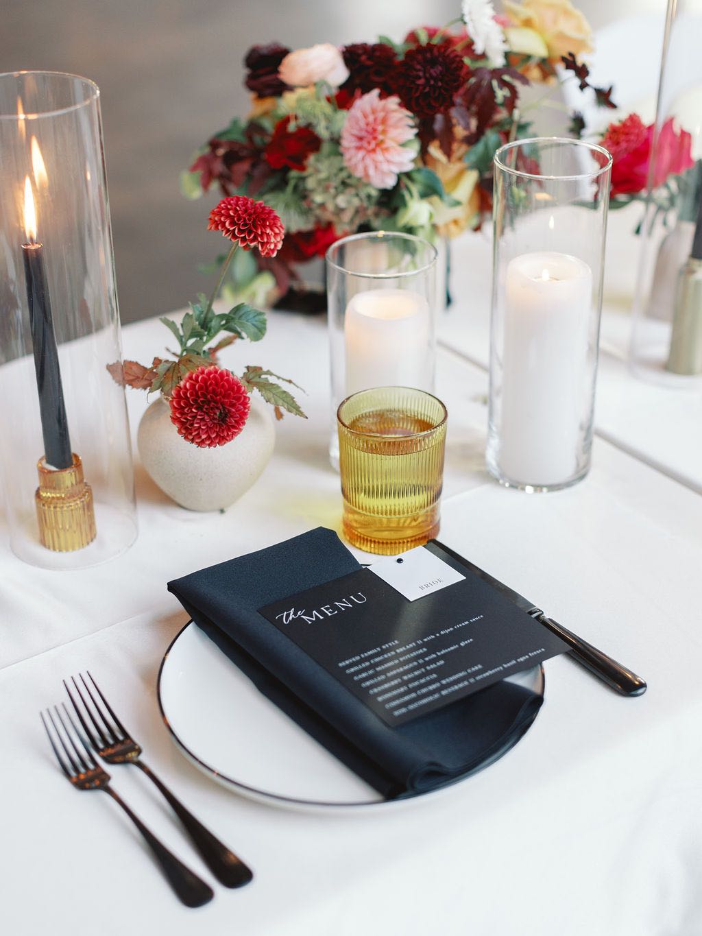 Wedding place setting with black napkin, menu and flatware and amber glassware