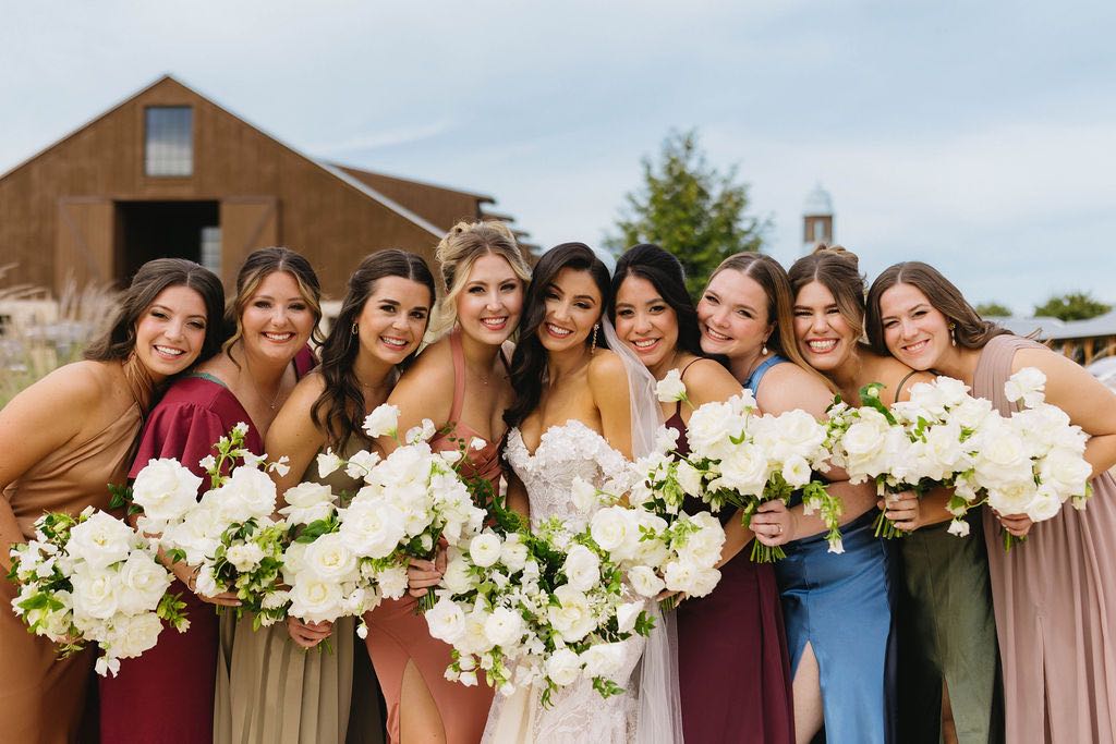 Bride with her bridesmaids, who are wearing colorful mismatched dresses and holding white bouquets