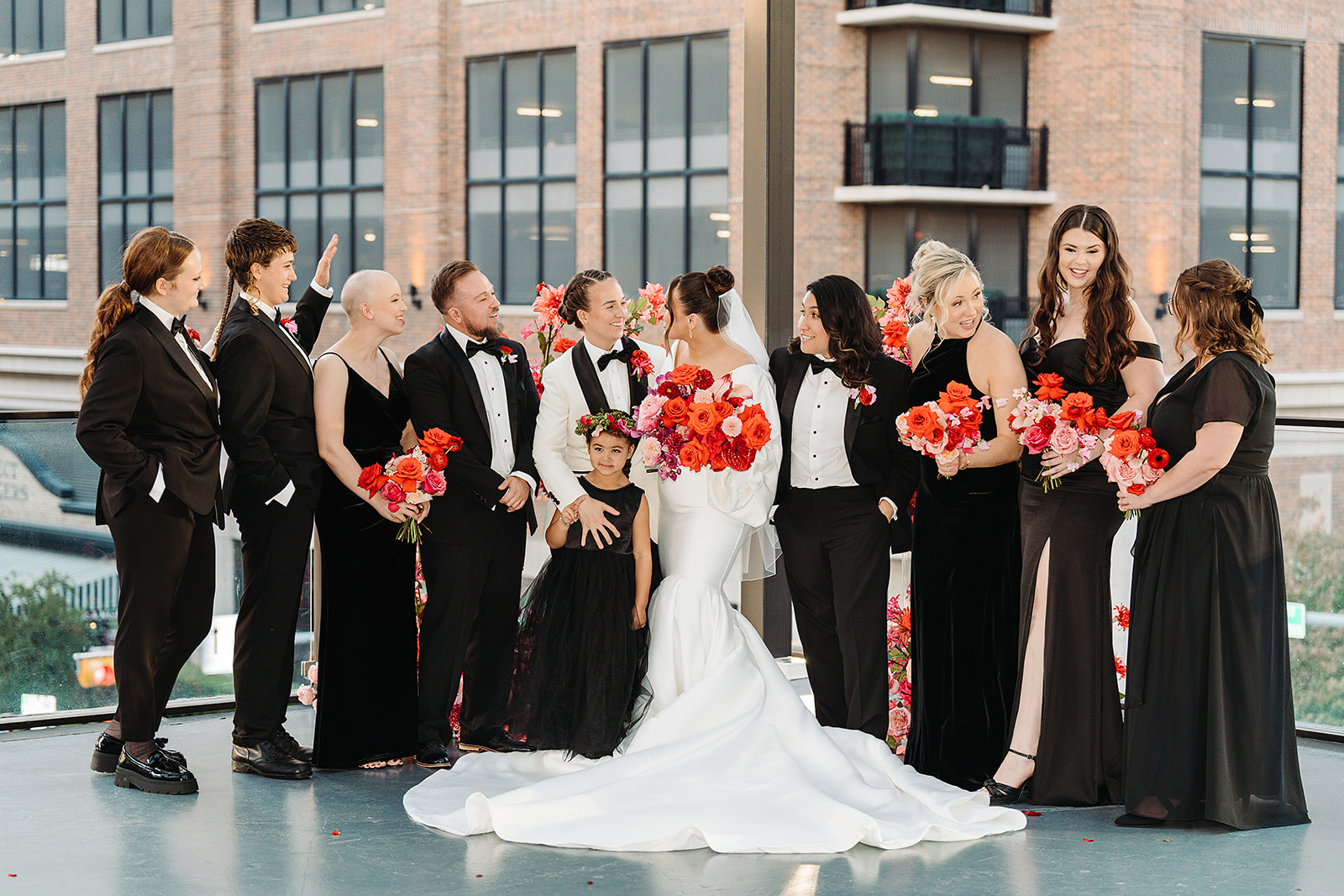 Wedding party wearing all black with brides, holding red and pink bouquets