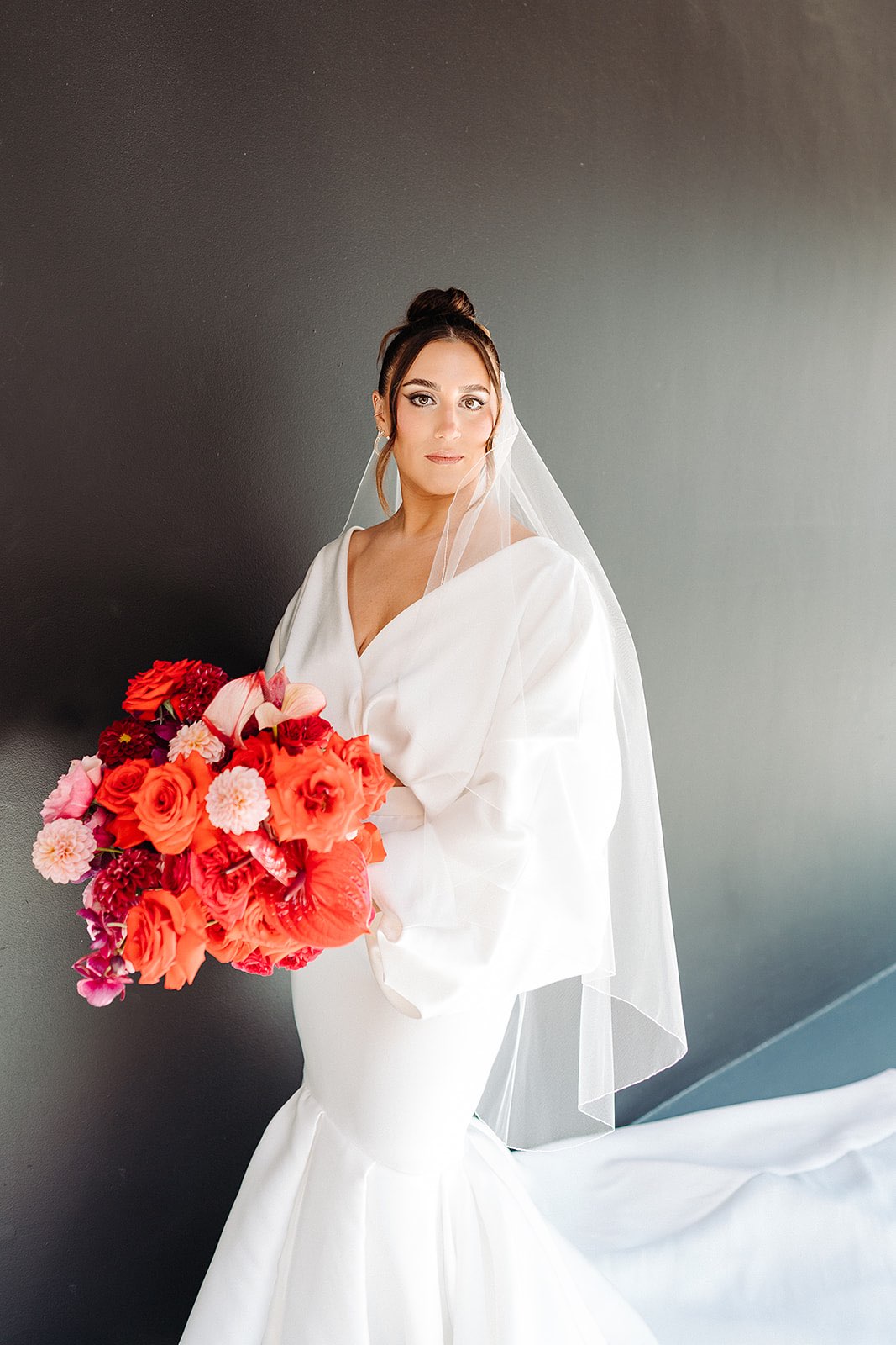Bride in trendy white two piece outfit holding bold red bouquet