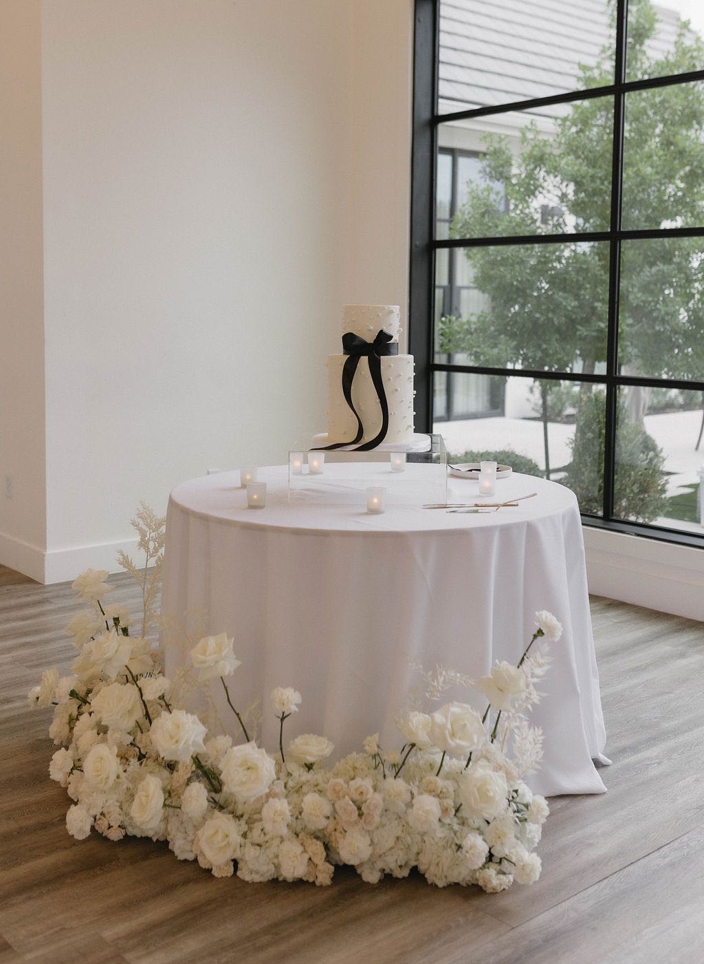 White wedding cake with black bow and grounded floral arrangements