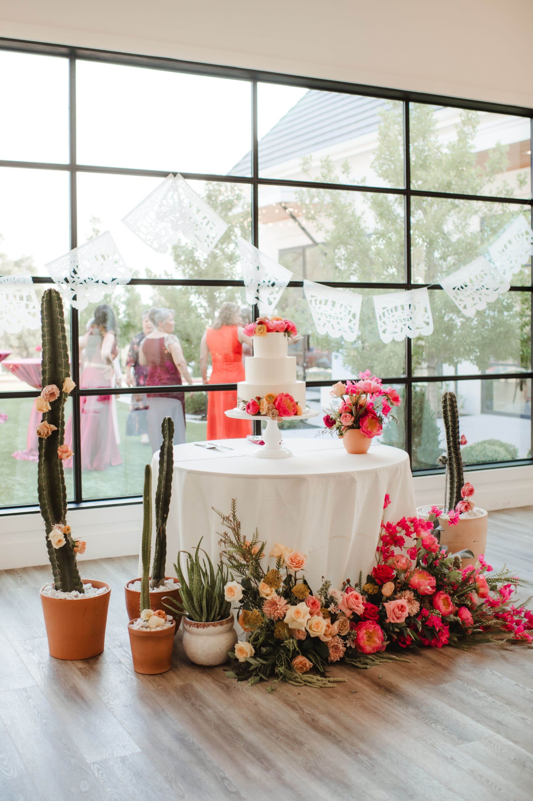 Summer wedding cake with bright pink flowers, cactus, and custom papel picado