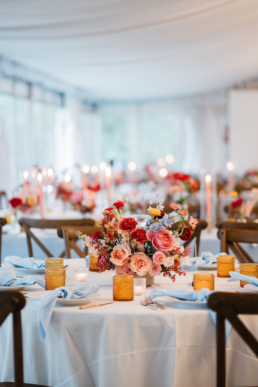 Wedding reception decor with white linen, blue napkins, peach, yellow, red and blush flowers. 