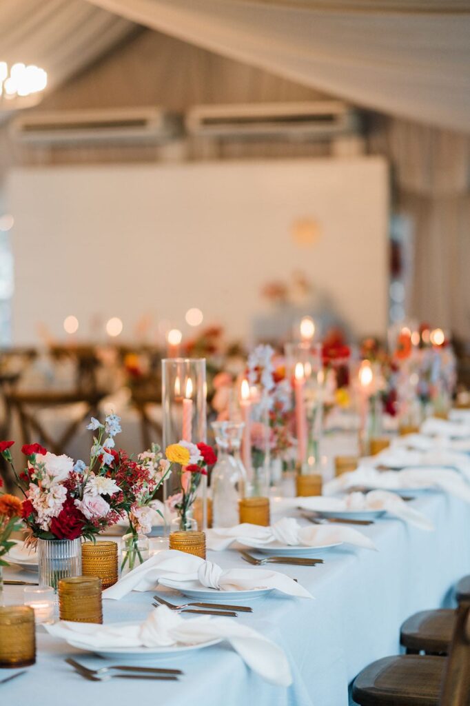 Wedding reception decor with light blue linen, white napkins, peach, yellow, red and blush flowers. 