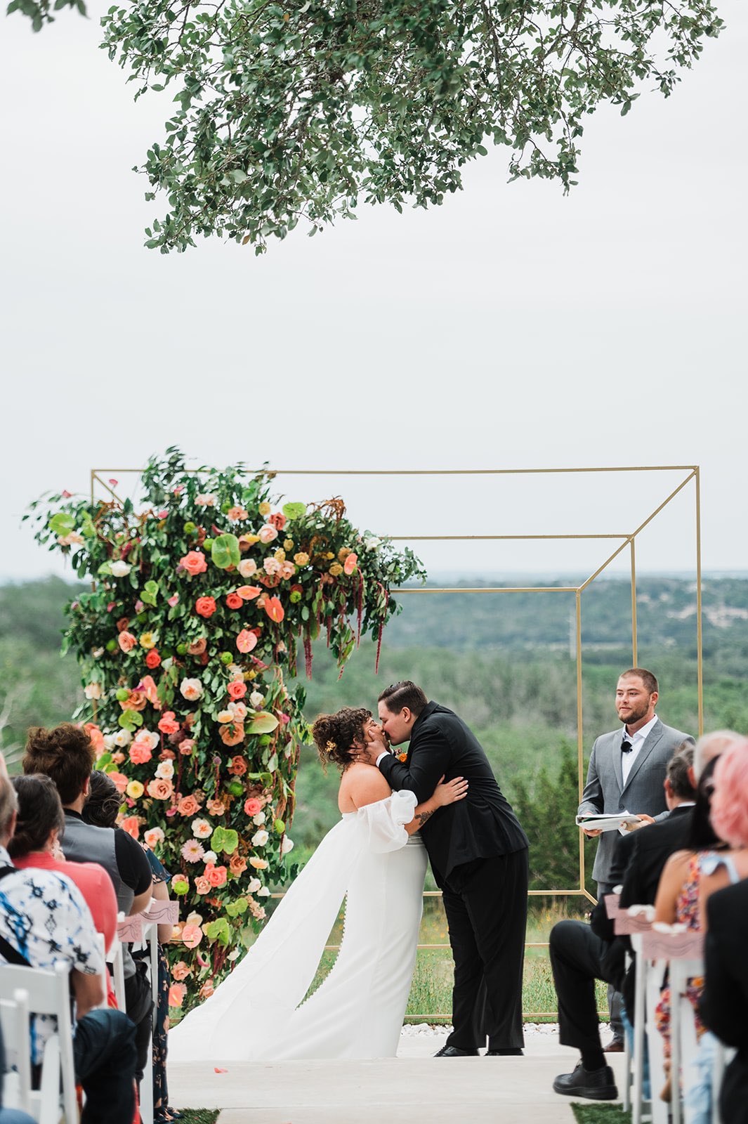 Couples first kiss in front of outdoor gold ceremony arch