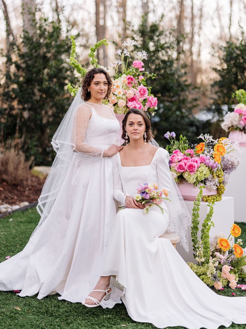 Two brides posed in front of colorful spring wedding ceremony decor